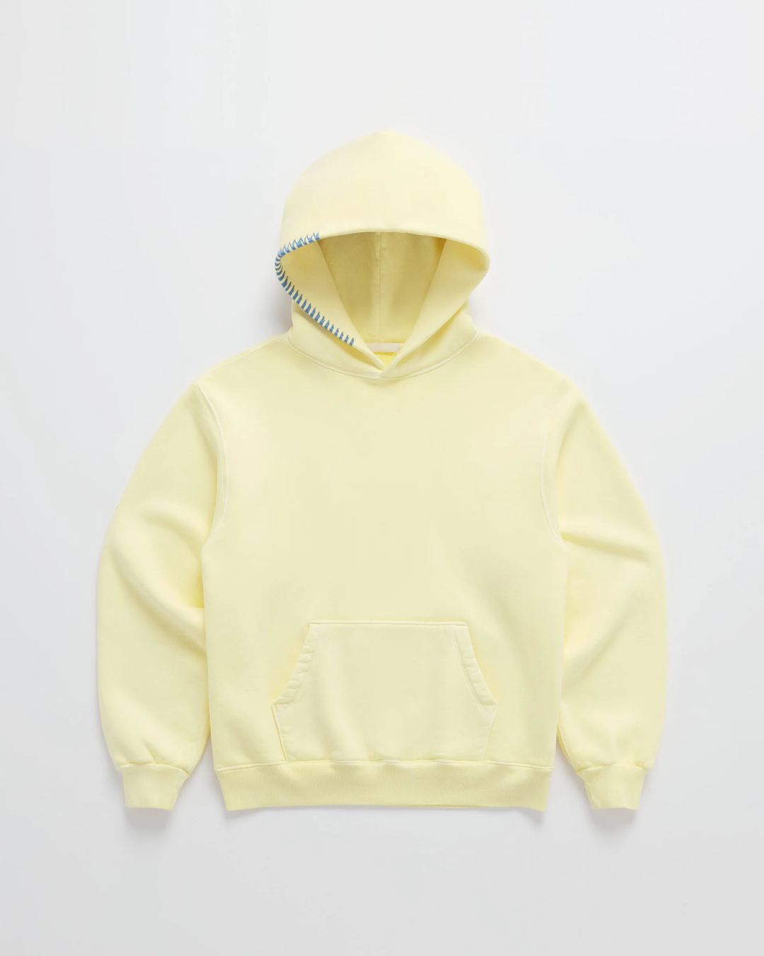 Sweat à capuche jaune pâle posé à plat, poche kangourou ventrale et couture bleue en zigzag sur le bord de la capuche. 1