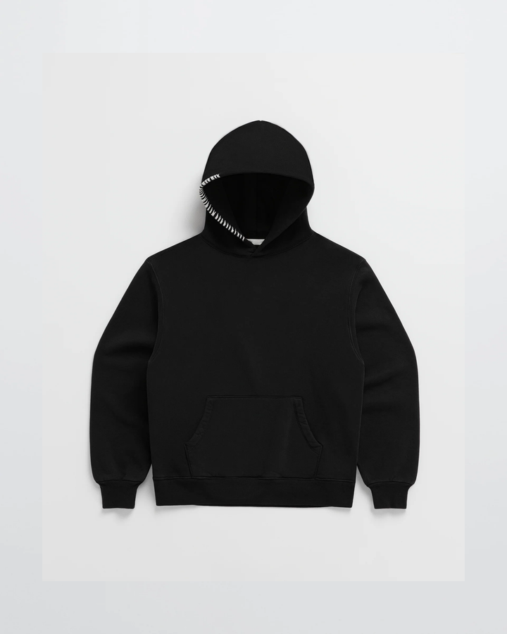 Sweat à capuche noir posé à plat, poche kangourou et couture blanche en zigzag sur le bord de la capuche. 5