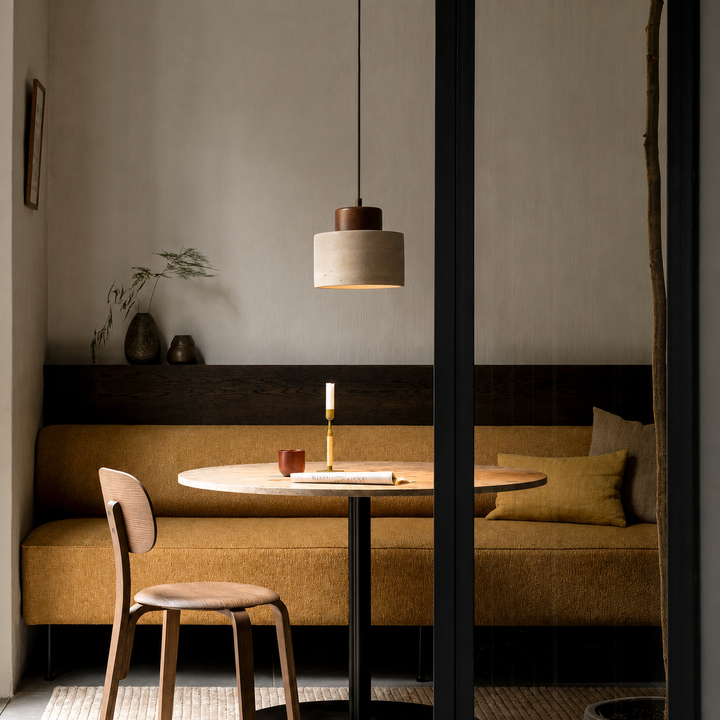 Suspension éclairant une table ronde devant une banquette ocre, dans une ambiance chaleureuse et tamisée 4