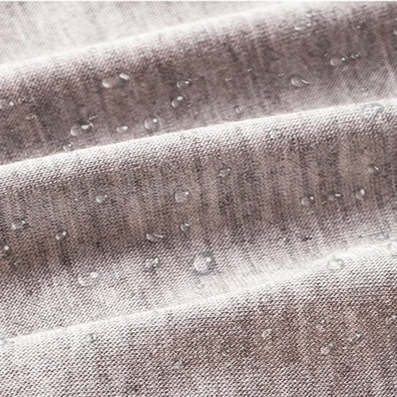 Gros plan sur un tissu gris chiné où perlent des gouttes d'eau, illustrant la couche imperméable. 9