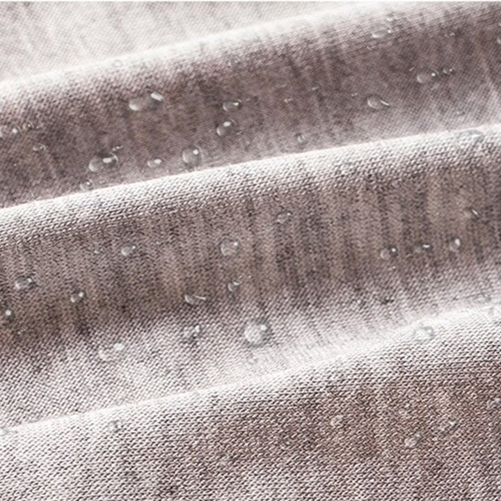 Gros plan sur un tissu gris chiné où perlent des gouttes d'eau, illustrant la couche imperméable. 9