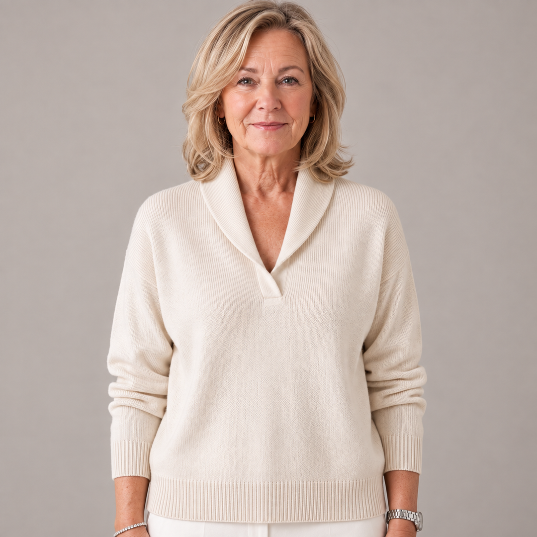 Femme au regard calme portant le pull couleur crème à col châle et bords côtelés, sur fond gris. 2