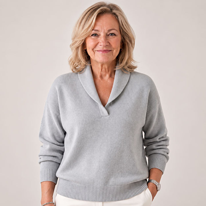 Femme souriante portant le pull gris clair à col châle, une main dans la poche d'un pantalon blanc. 3