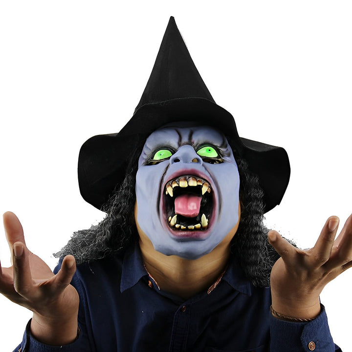 Masque de sorcière au visage bleuté, yeux verts et bouche hurlante, porté avec un chapeau pointu noir et des cheveux bouclés. 22