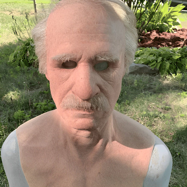 Masque de vieil homme avec moustache et cheveux gris, photographié en extérieur dans un jardin, buste moulé visible. 7