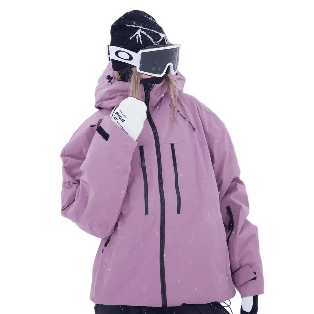 Gros plan de la veste rose mauve portée avec bonnet noir et masque de ski, une main gantée de blanc remontée vers le menton. 2