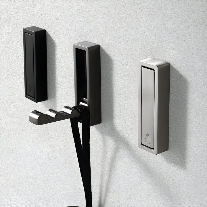 Trois crochets rectangulaires noir et argenté sur mur texturé gris, dont un déplié retenant des lanières noires. 13