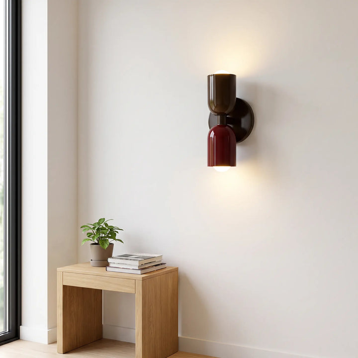 Applique brun foncé et bordeaux allumée sur mur blanc, au-dessus d'une petite table en bois avec plante et livres. 10