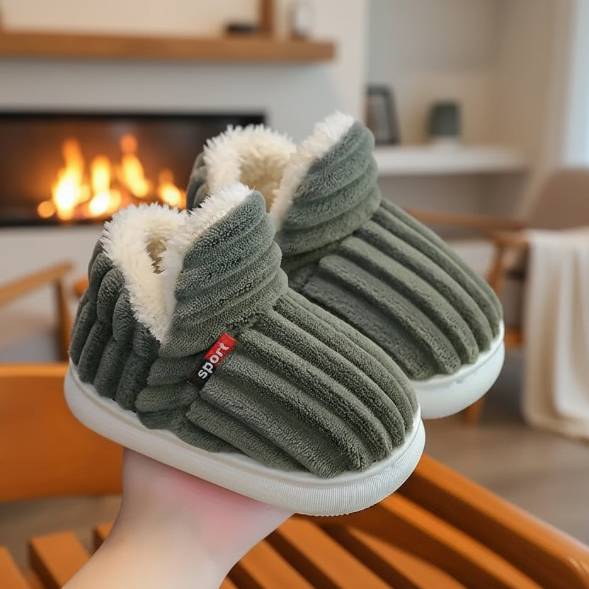 Paire de chaussons vert kaki côtelés à doublure peluche, tenue en main devant une cheminée allumée. 6