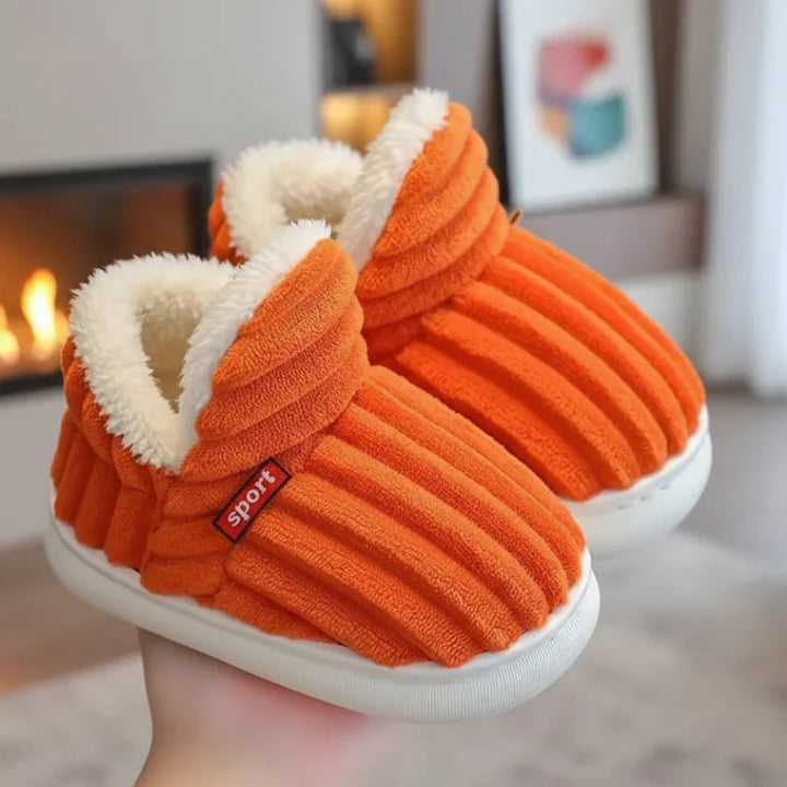 Paire de chaussons orange côtelés à doublure en fourrure blanche, tenue en main près d'une cheminée. 8