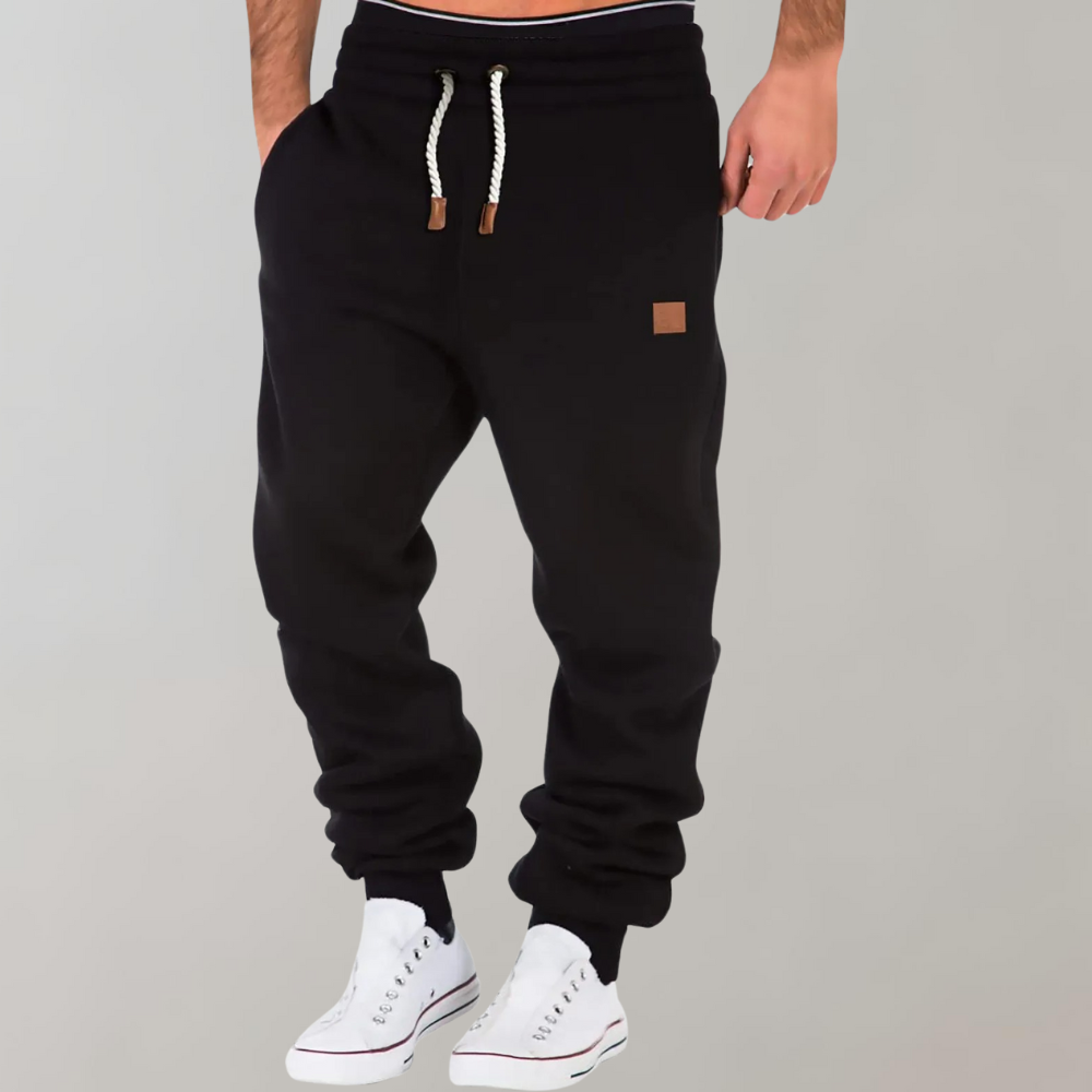 Jogging noir porté par un homme avec baskets blanches, cordon blanc et petit patch marron 1