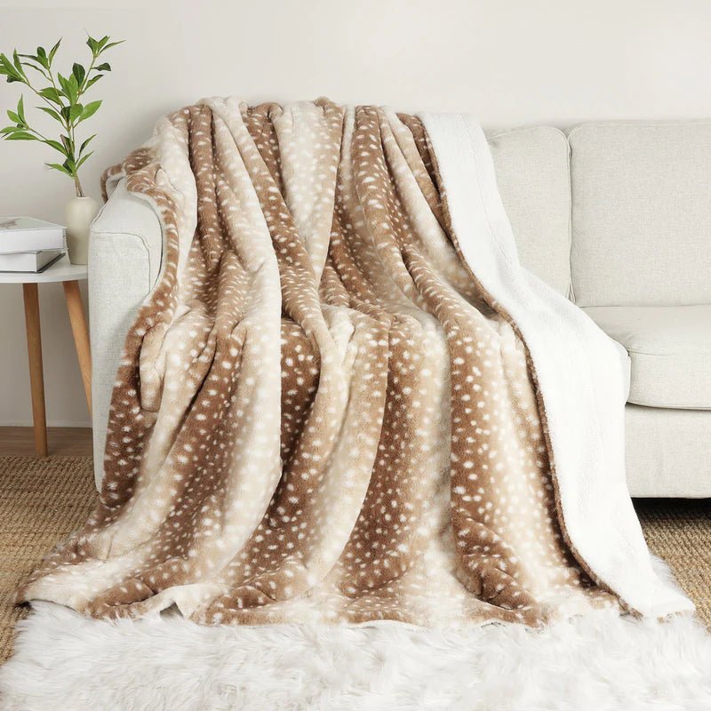 Couverture beige et marron tachetée de blanc, drapée sur un canapé clair avec son envers blanc duveteux visible sur le côté. 1