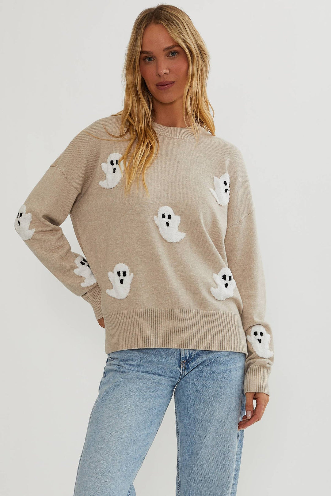 Femme blonde portant le pull beige à petits fantômes blancs duveteux, porté avec un jean bleu clair, vue de face. 1