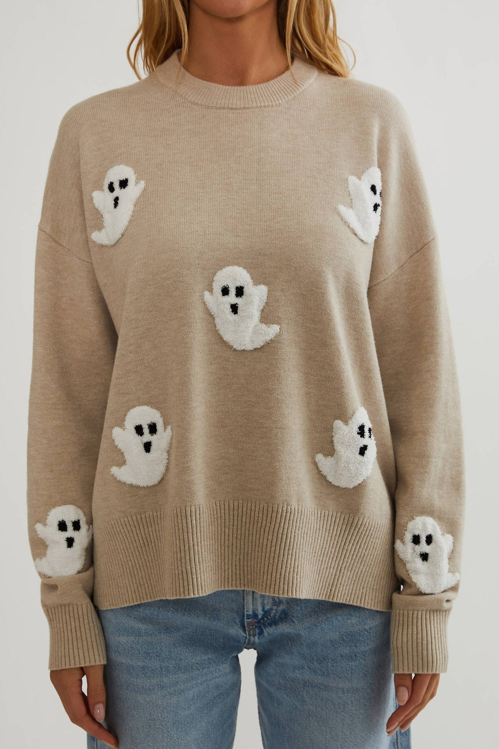 Gros plan de face sur le pull beige en maille fine, avec ses fantômes blancs texturés et ses bords côtelés. 2