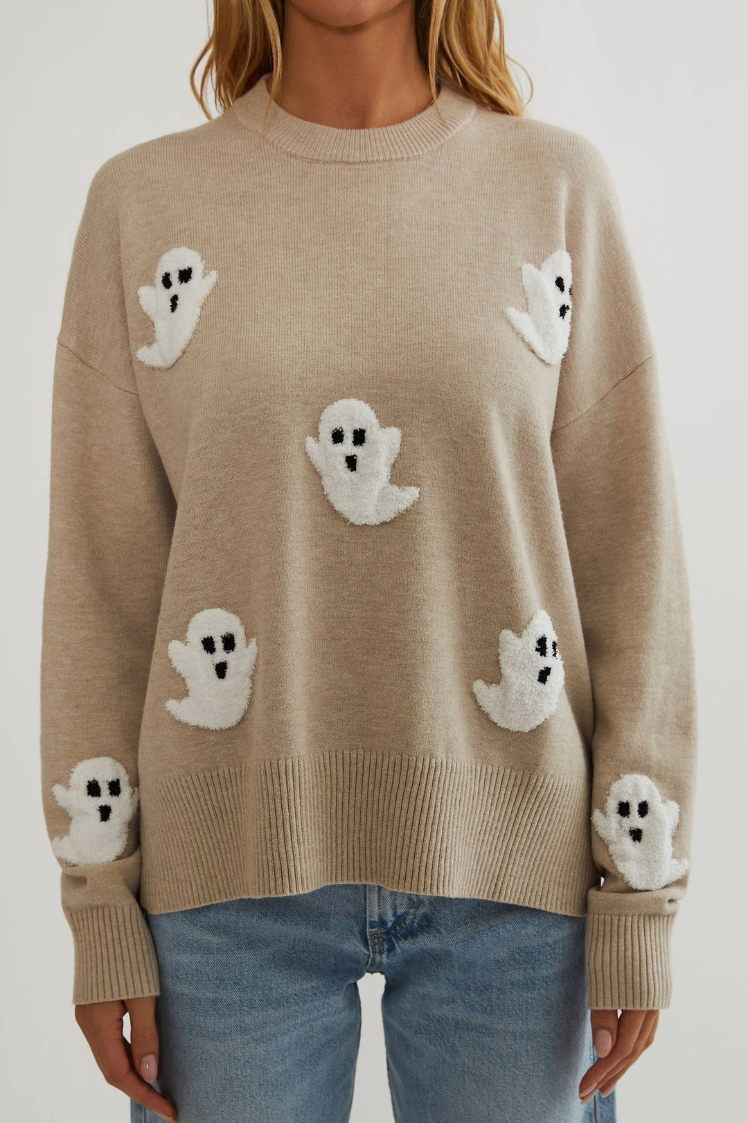 Gros plan de face sur le pull beige en maille fine, avec ses fantômes blancs texturés et ses bords côtelés. 2