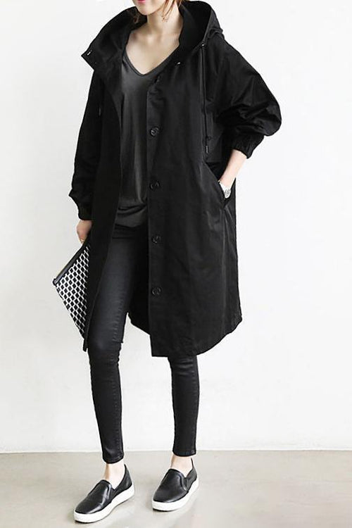 Manteau noir porté ouvert sur un tee-shirt, avec leggings, baskets et pochette, une main dans la poche 2