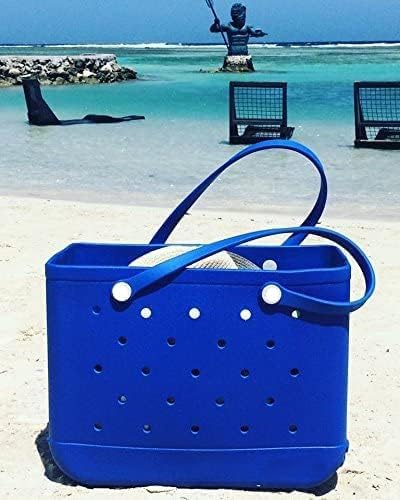 Sac cabas bleu vif posé sur le sable d'une plage, avec un chapeau de paille dépassant, mer turquoise en arrière-plan. 23