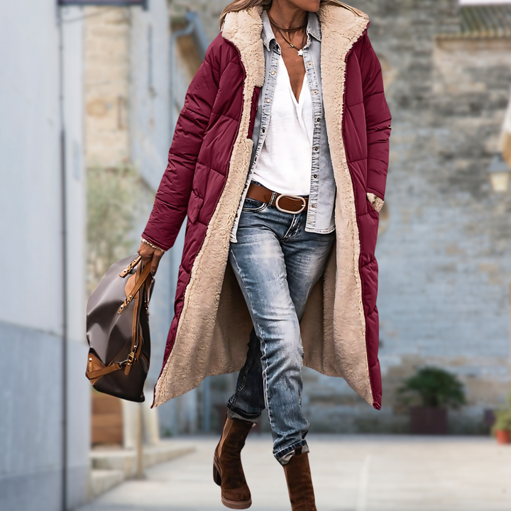 Femme en extérieur portant une longue veste matelassée bordeaux ouverte, doublée de peluche beige, avec chemise en jean et sac à main. 6