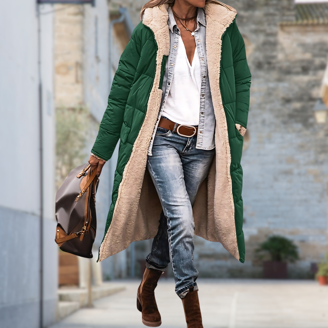 Femme marchant en ville avec une longue veste matelassée verte ouverte, doublure en peluche beige, jean, bottines et sac marron. 7