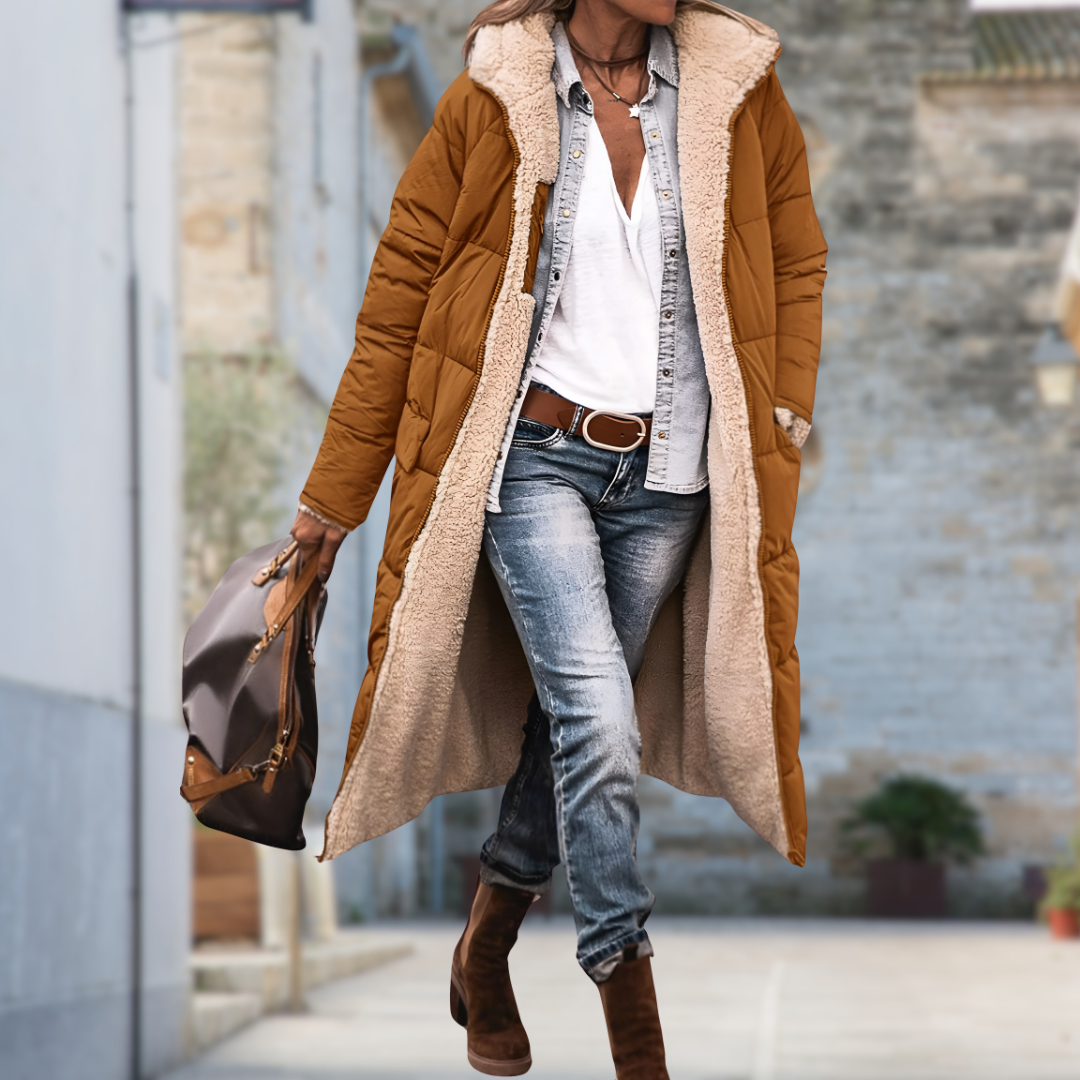 Femme dans une ruelle portant une longue veste matelassée marron caramel ouverte, doublée de peluche beige, avec jean et sac à main. 9