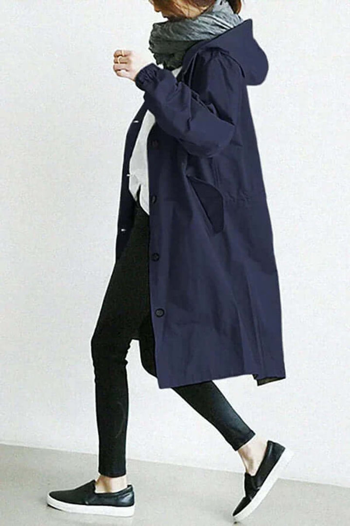 Trench bleu marine à capuche vu de profil en marche, avec jean noir et baskets 8