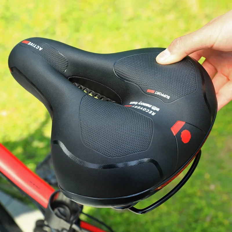 Main tenant la selle noire à zones texturées antidérapantes, avec un cadre de vélo rouge au second plan sur l'herbe. 5