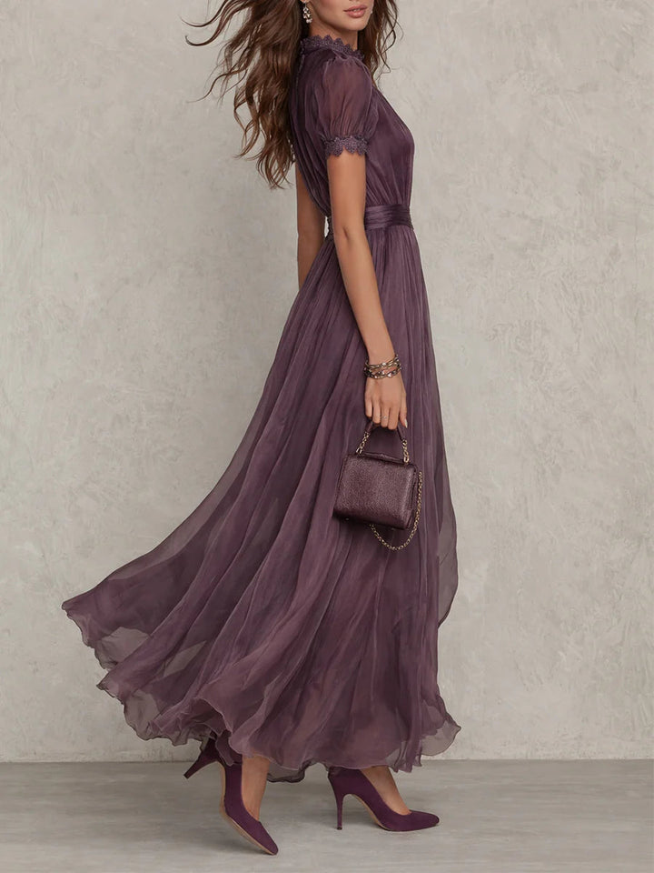 Robe longue prune portée de profil, montrant les manches courtes bordées de dentelle, la taille froncée et la jupe légère qui flotte. 2