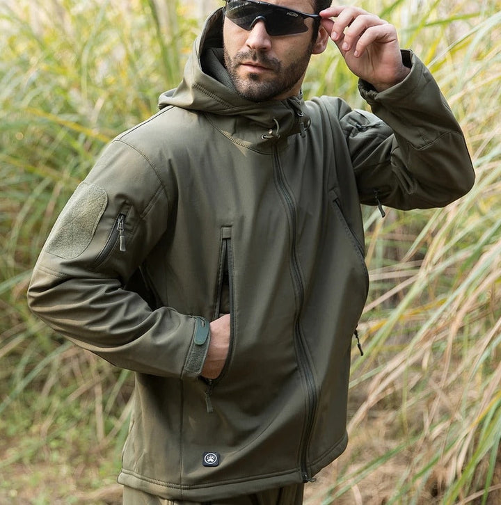 Homme en lunettes de soleil portant la veste vert olive dans de hautes herbes, une main dans la poche zippée. 11