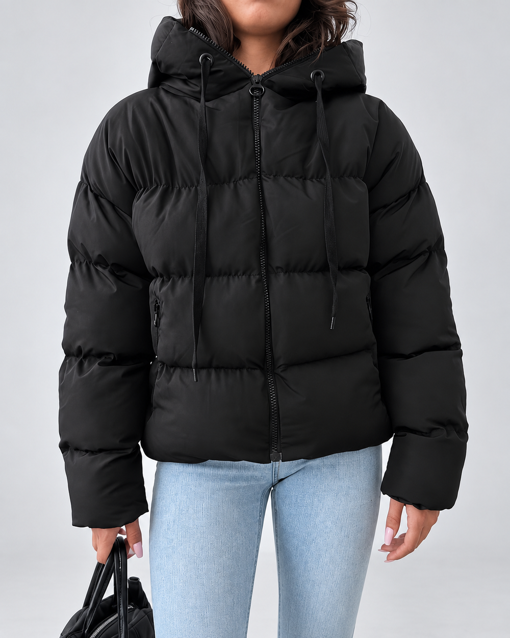 Vue de face de la veste noire zippée, avec capuche à cordons de serrage et poches zippées sur le devant, portée avec un jean. 2