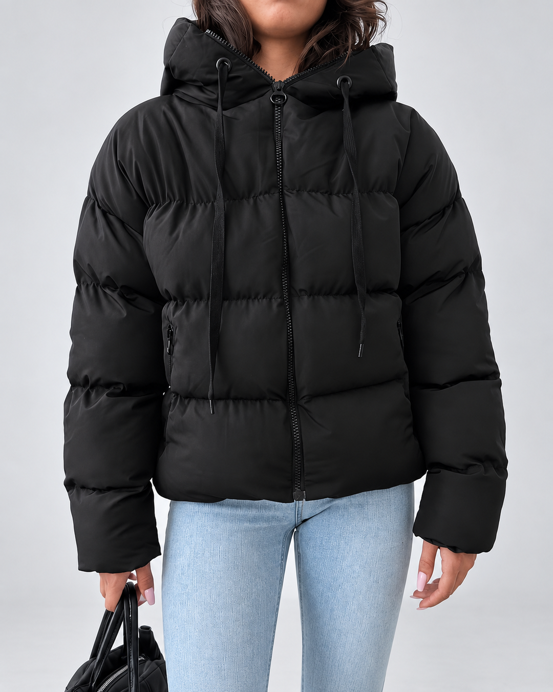 Vue de face de la veste noire zippée, avec capuche à cordons de serrage et poches zippées sur le devant, portée avec un jean. 2