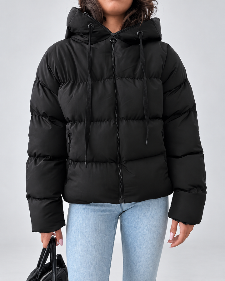 Vue de face de la veste noire zippée, avec capuche à cordons de serrage et poches zippées sur le devant, portée avec un jean. 2