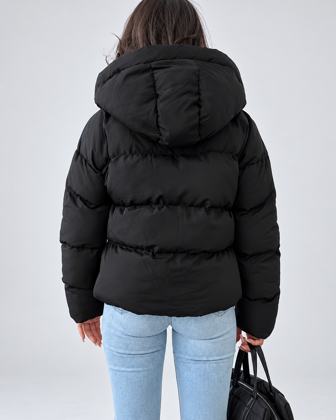 Vue de dos de la veste matelassée noire portée par une femme, avec la capuche matelassée et un jean clair. 3